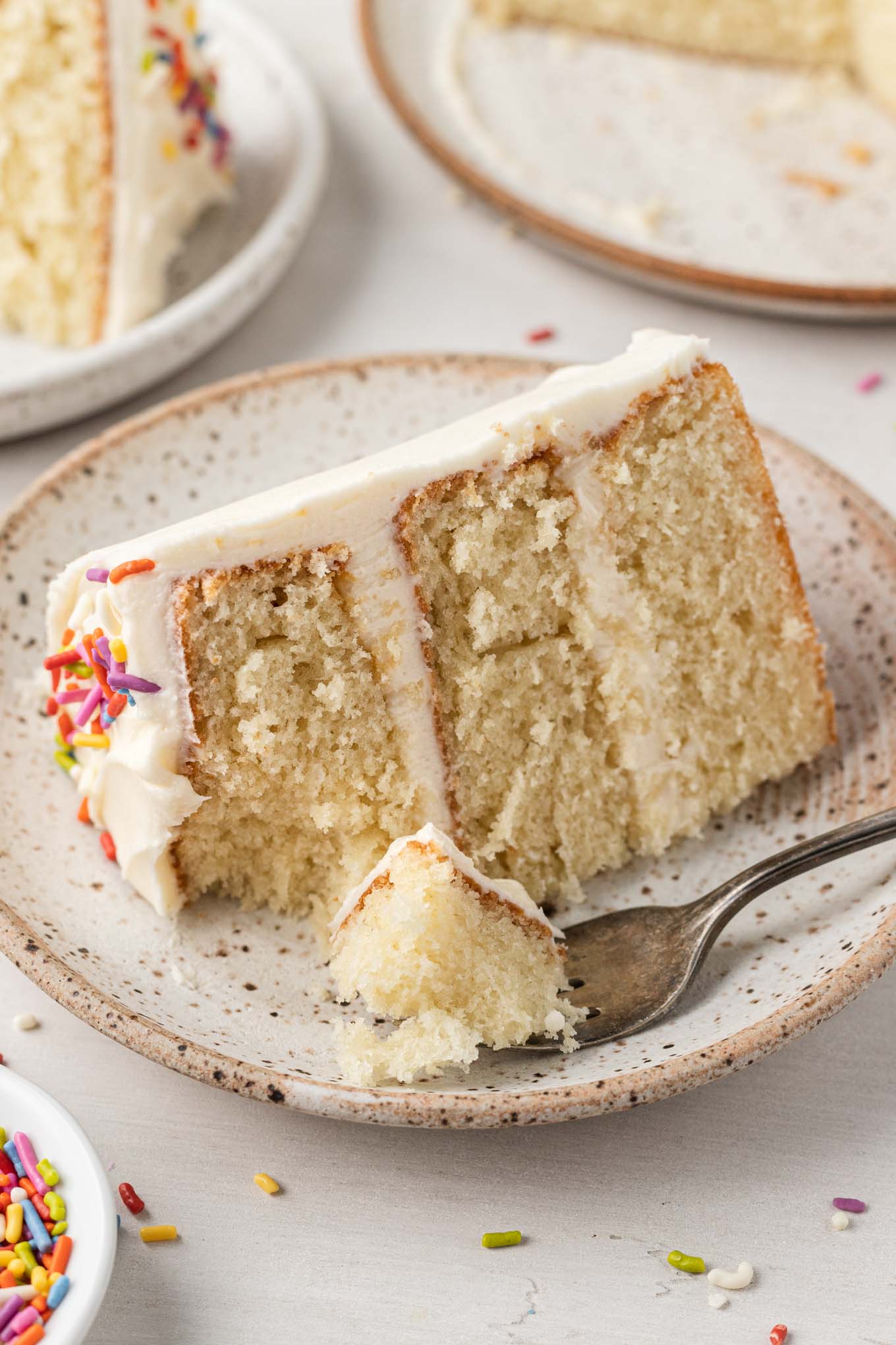 A slice of mini vanilla cake on a speckled white dessert plate. 
