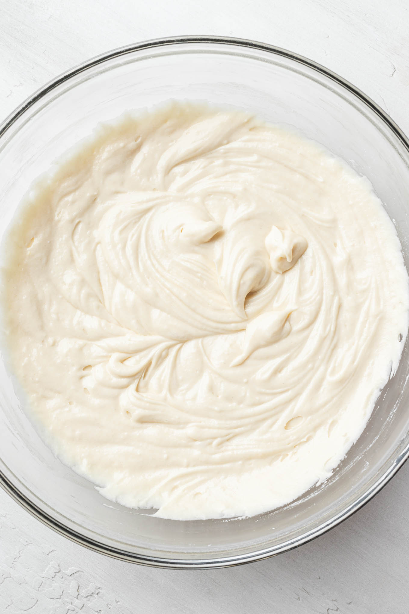 An overhead view of vanilla cake batter in a glass mixing bowl.