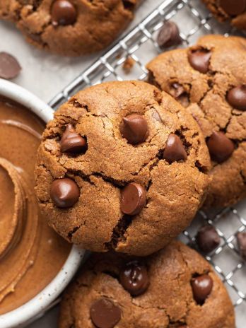 Several almond butter cookies on a wire rack. A bowl of almond butter is next to the cookies.