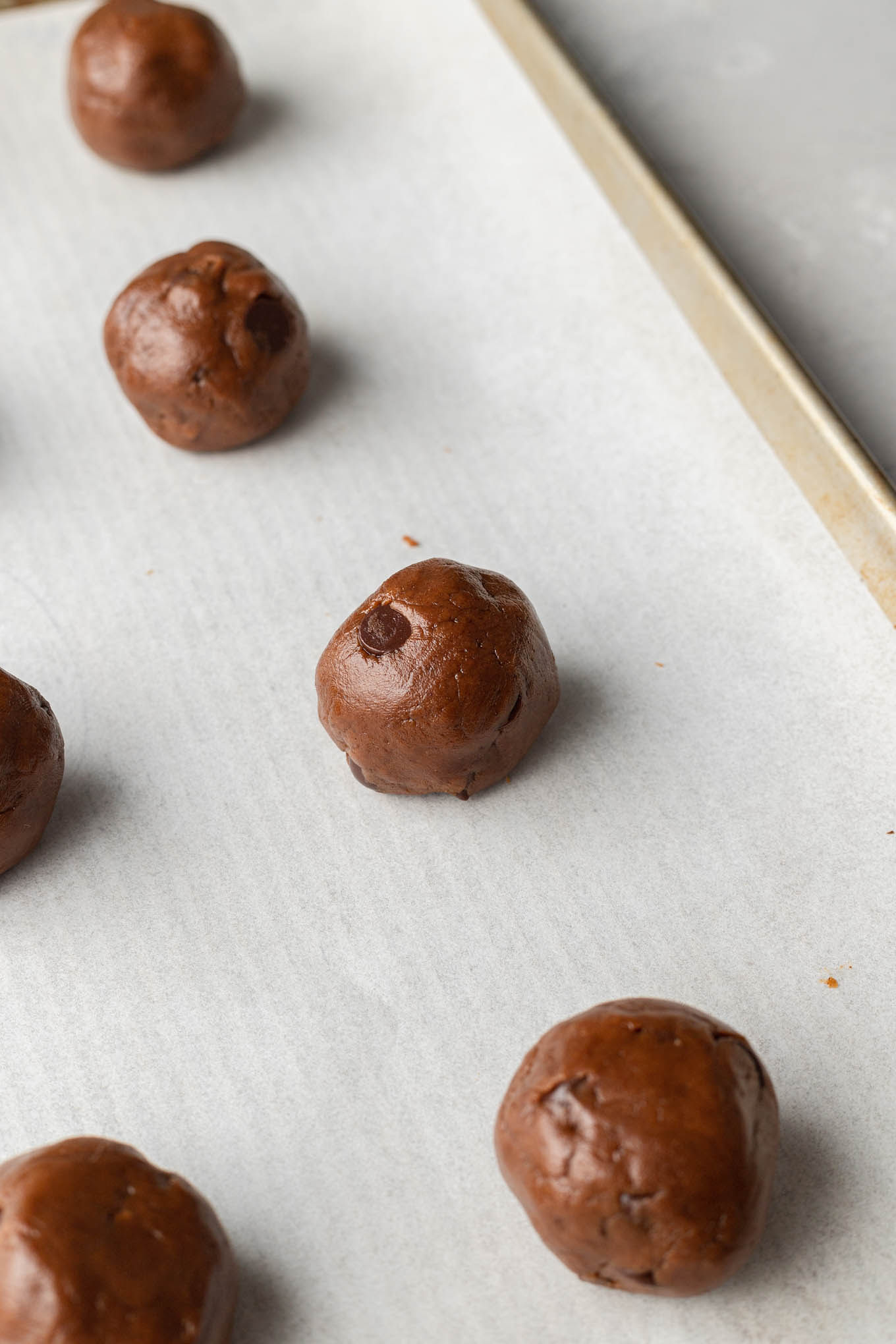 Almond butter cookie dough balls on a parchment paper-lined baking sheet. 