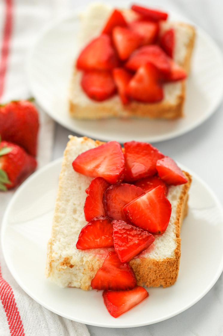 Sliced angel food cake on white plates topped with sliced strawberries.