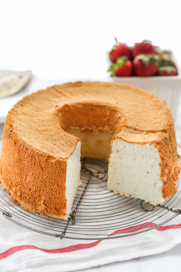 An angel food cake on top of a wire rack with strawberries in the background.