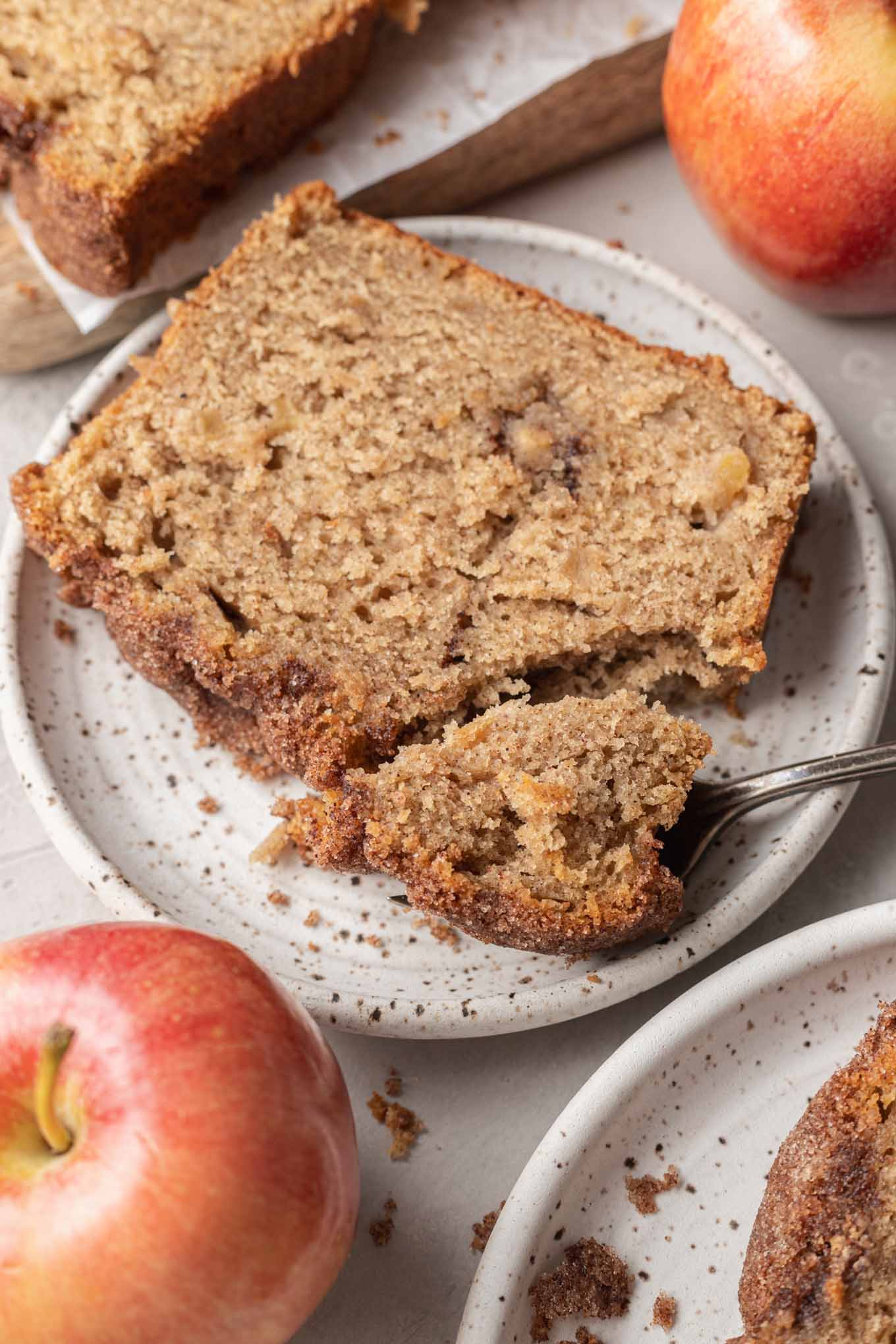 A slice of apple bread on a speckled dessert plate, with a fork. 