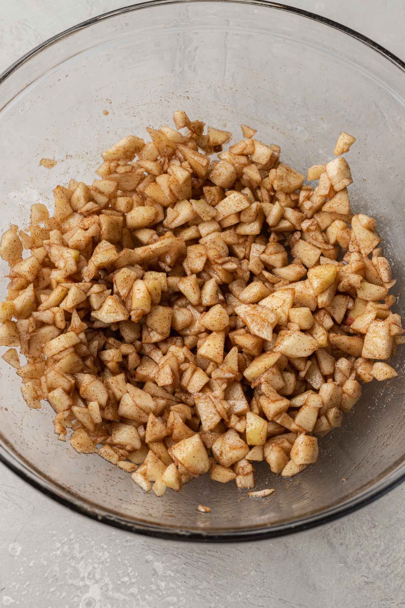 An overhead view of chopped apples in a glass mixing bowl. 