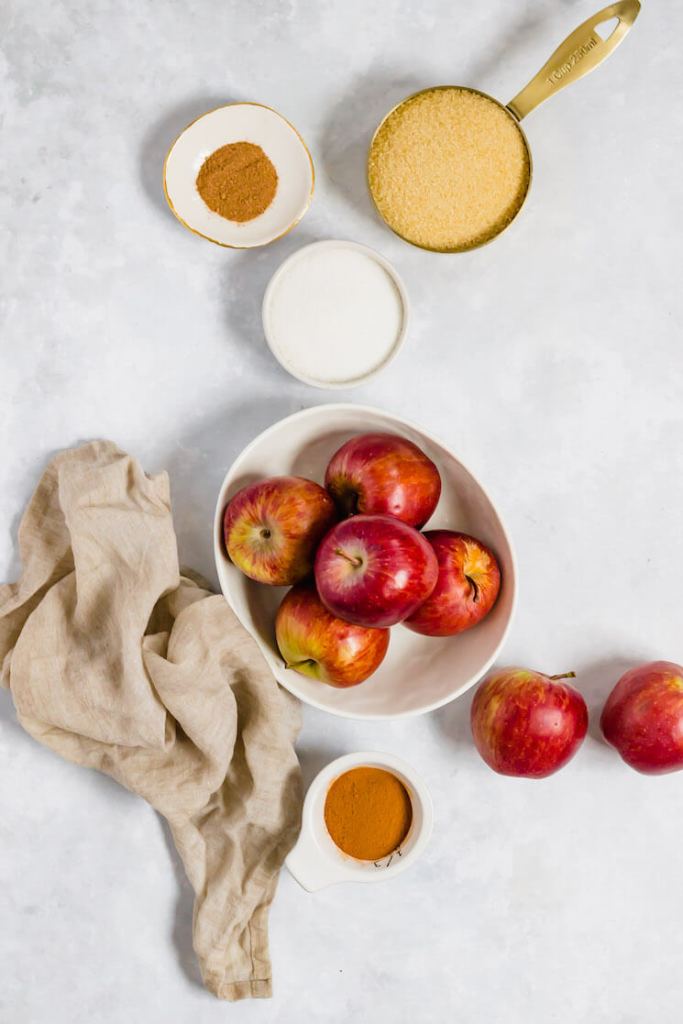 The ingredients needed to make apple butter in various bowls and measuring cups on a gray surface.