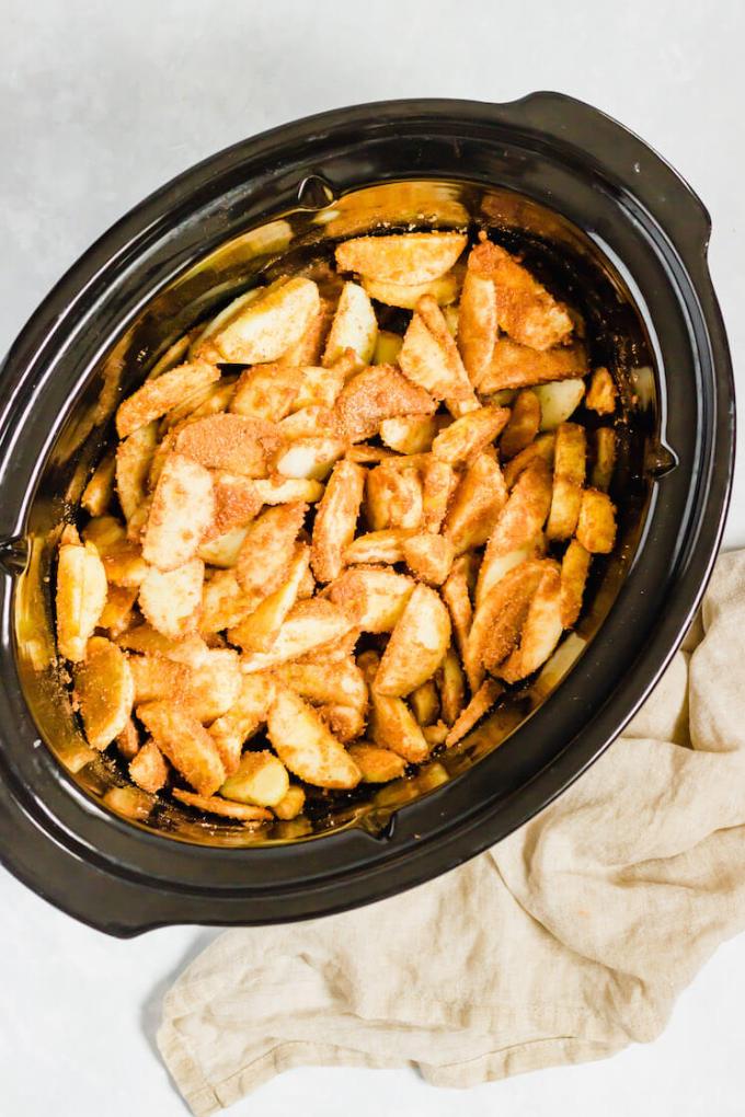 A crockpot filled with sliced apples that have been mixed with sugar and spices.