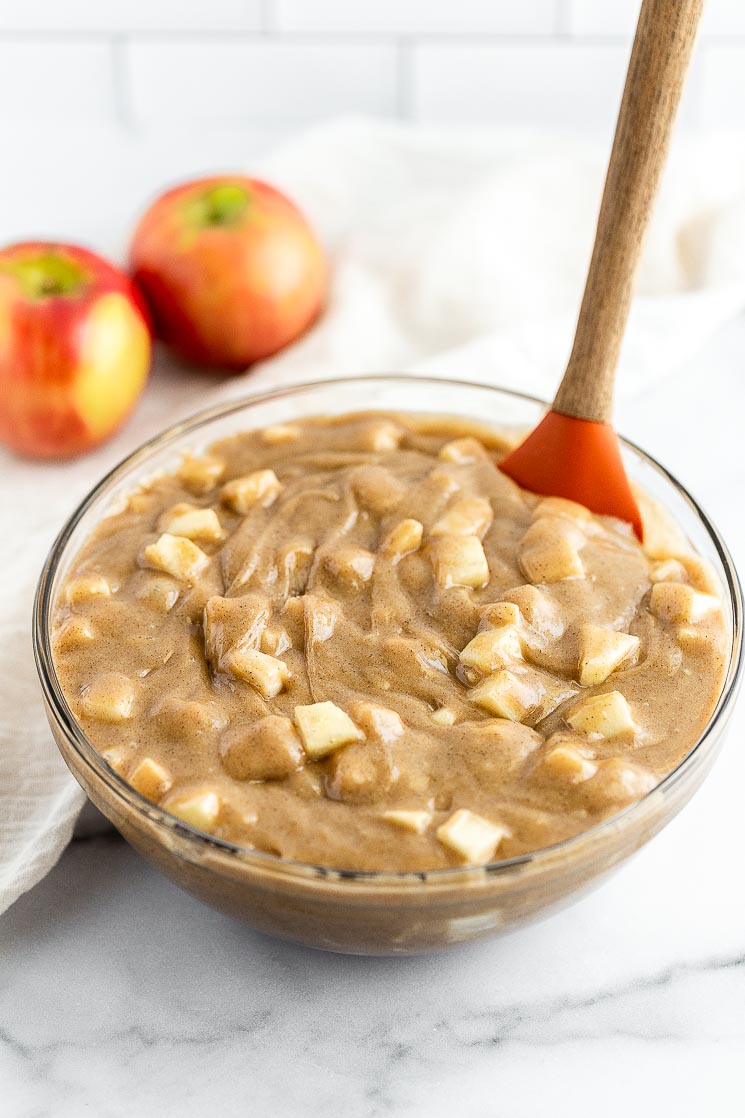 A glass bowl filled with cake batter and freshly chopped apples.