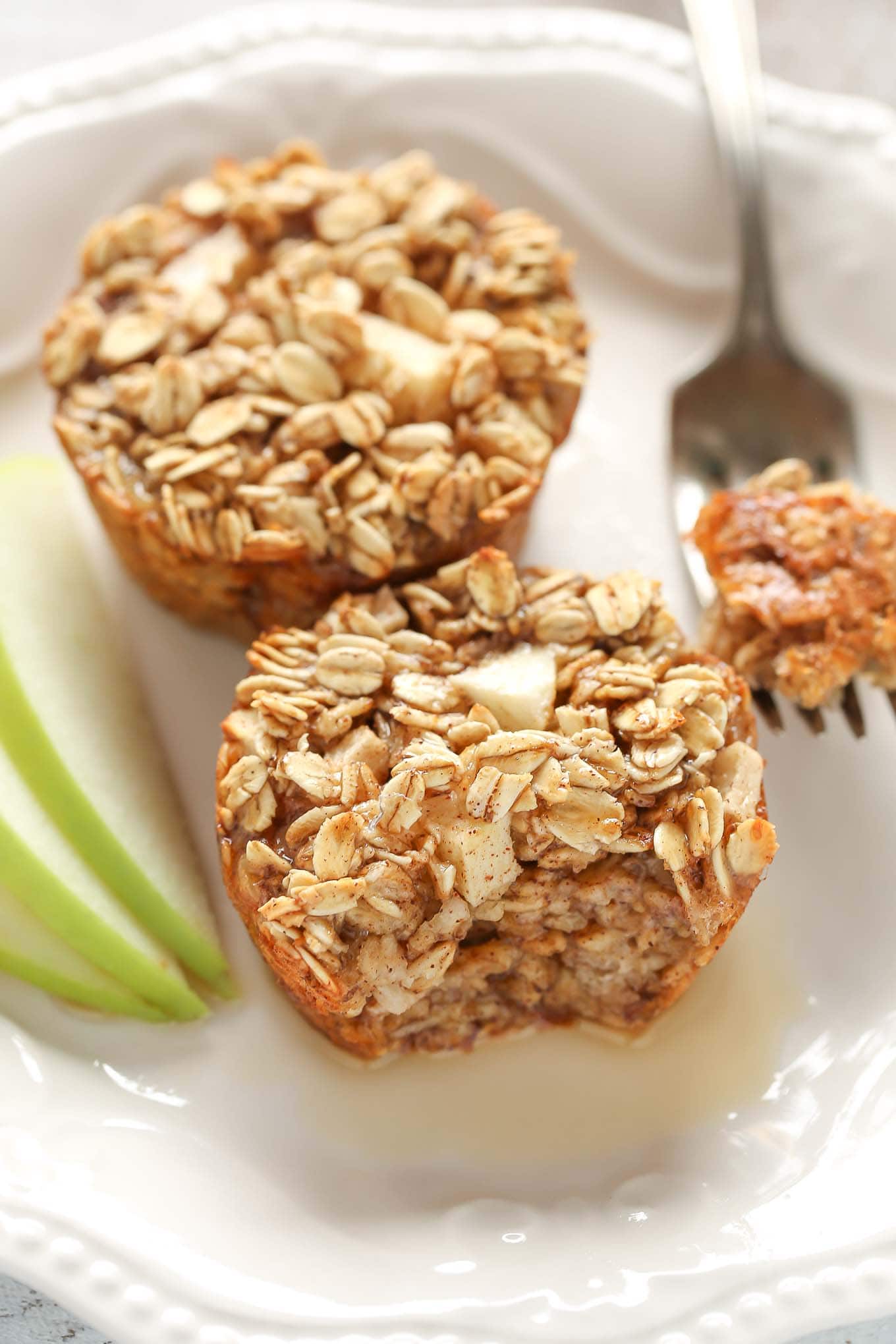 Two apple cinnamon baked oatmeal cups on a white plate with a fork and apple slices. 