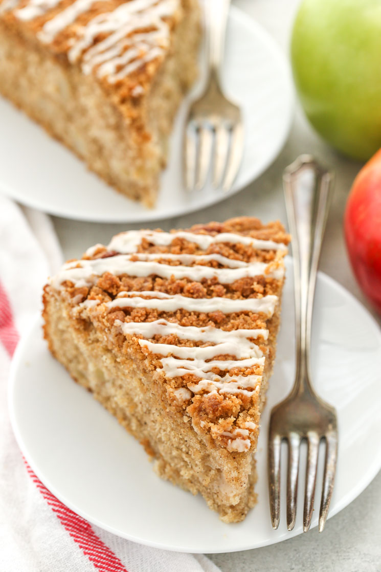 Two slices of apple coffee cake on white plates with forks. 