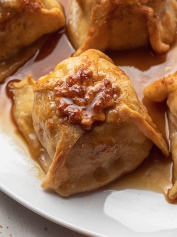 Four baked apple dumplings on a large white plate. The dumplings have been drizzled with extra sauce from the pan.