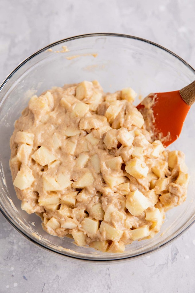 An overhead view of apple fritter dough in a glass mixing bowl with a rubber spatula.