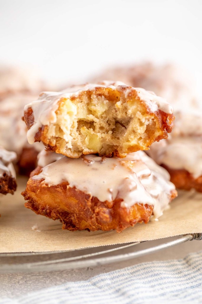 Two apple fritters, stacked on top of each other. The top fritter has a bite missing. 