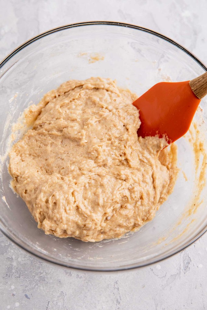 An overhead view of apple fritter dough in a glass mixing bowl with a rubber spatula.