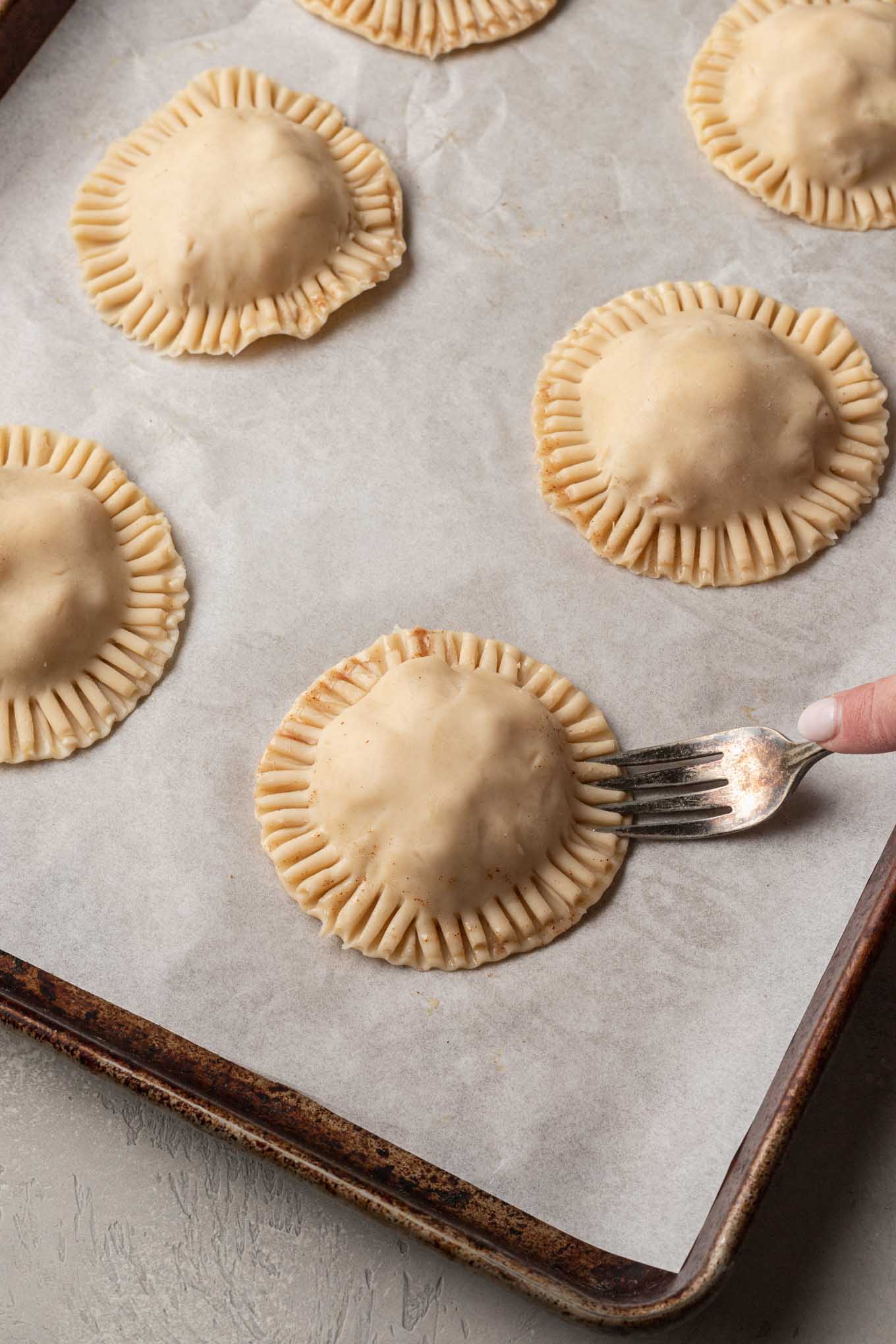A process shot showing the edges of mini apple hand pies being crimped together with a fork. 