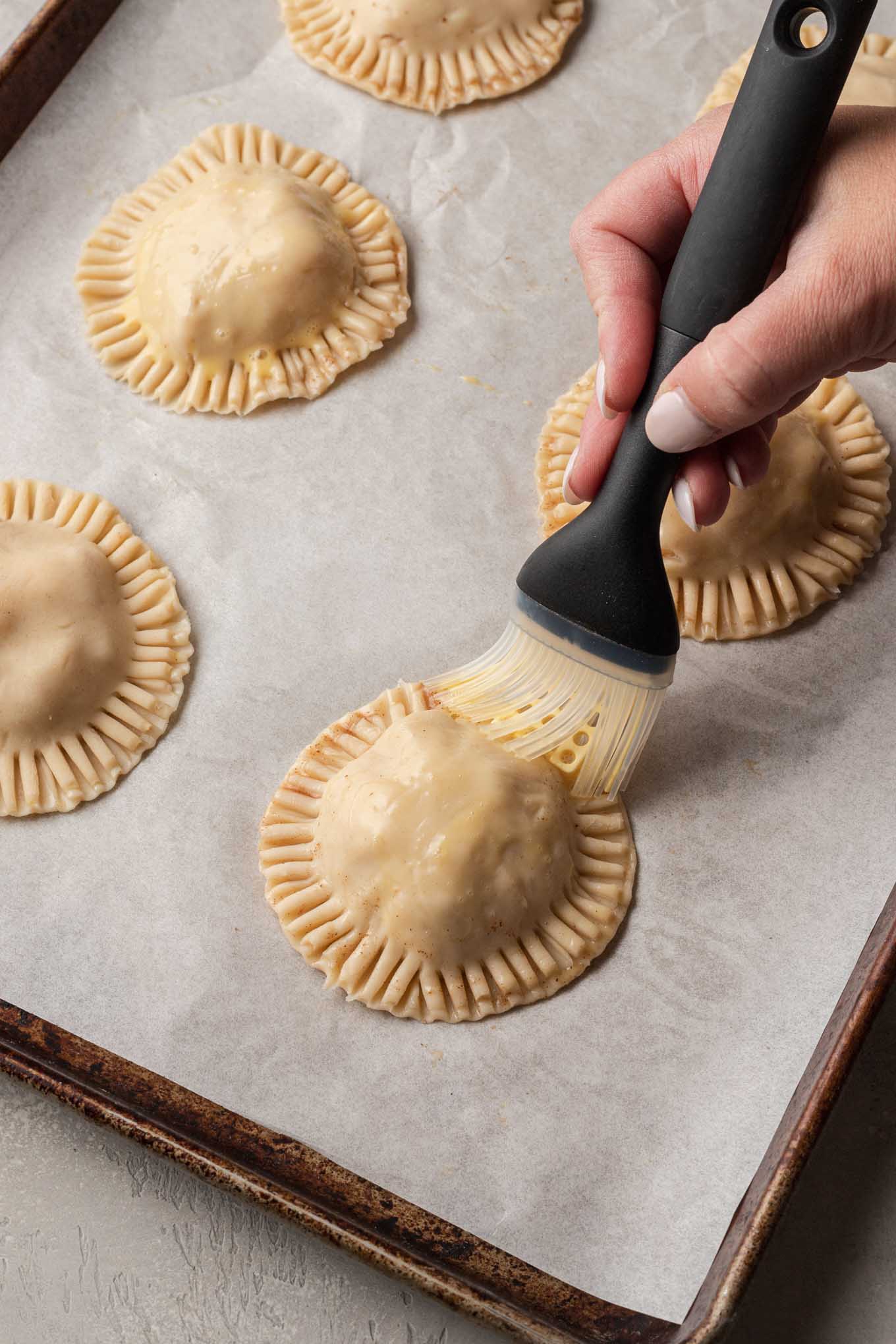 A process shot showing hand pies being brushed with an egg wash. 