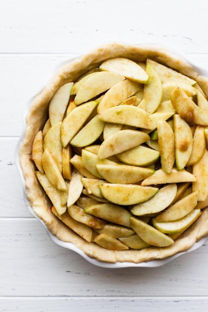 A white pie dish holding a pie crust filled with seasoned sliced apples.