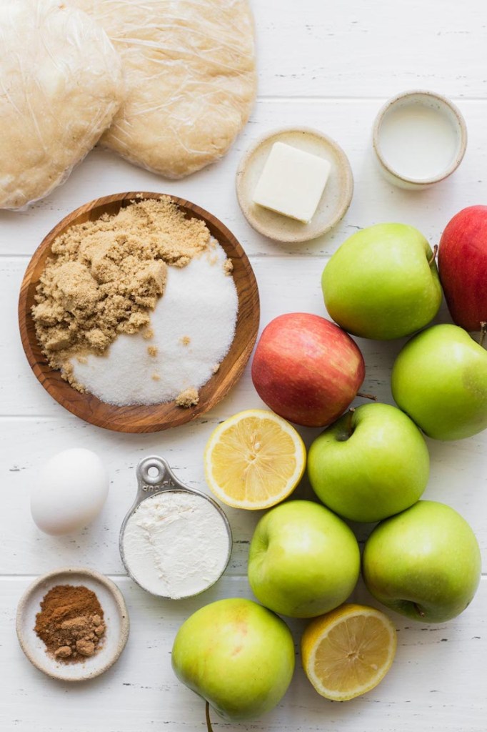 The ingredients needed to make apple pie sitting on top of a white surface.