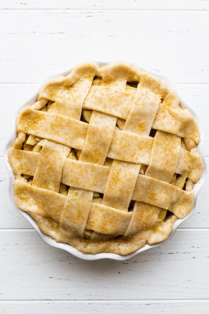 An apple pie topped with a lattice crust and coarse sugar ready to go into the oven.