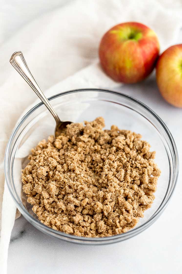 A bowl filled with streusel topping and apples in the background.