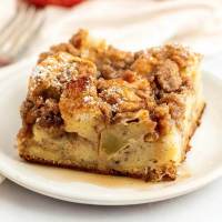 A slice of apple streusel french toast casserole topped with pure maple syrup on a white plate.