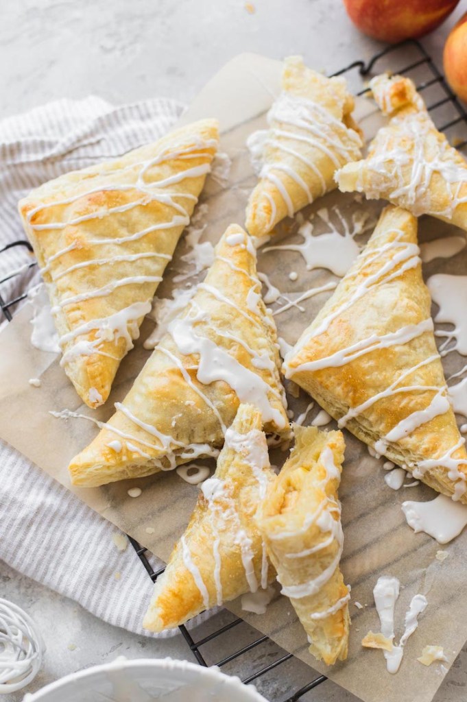 A batch of turnovers arranged on a cooling rack and topped with a maple cinnamon glaze.