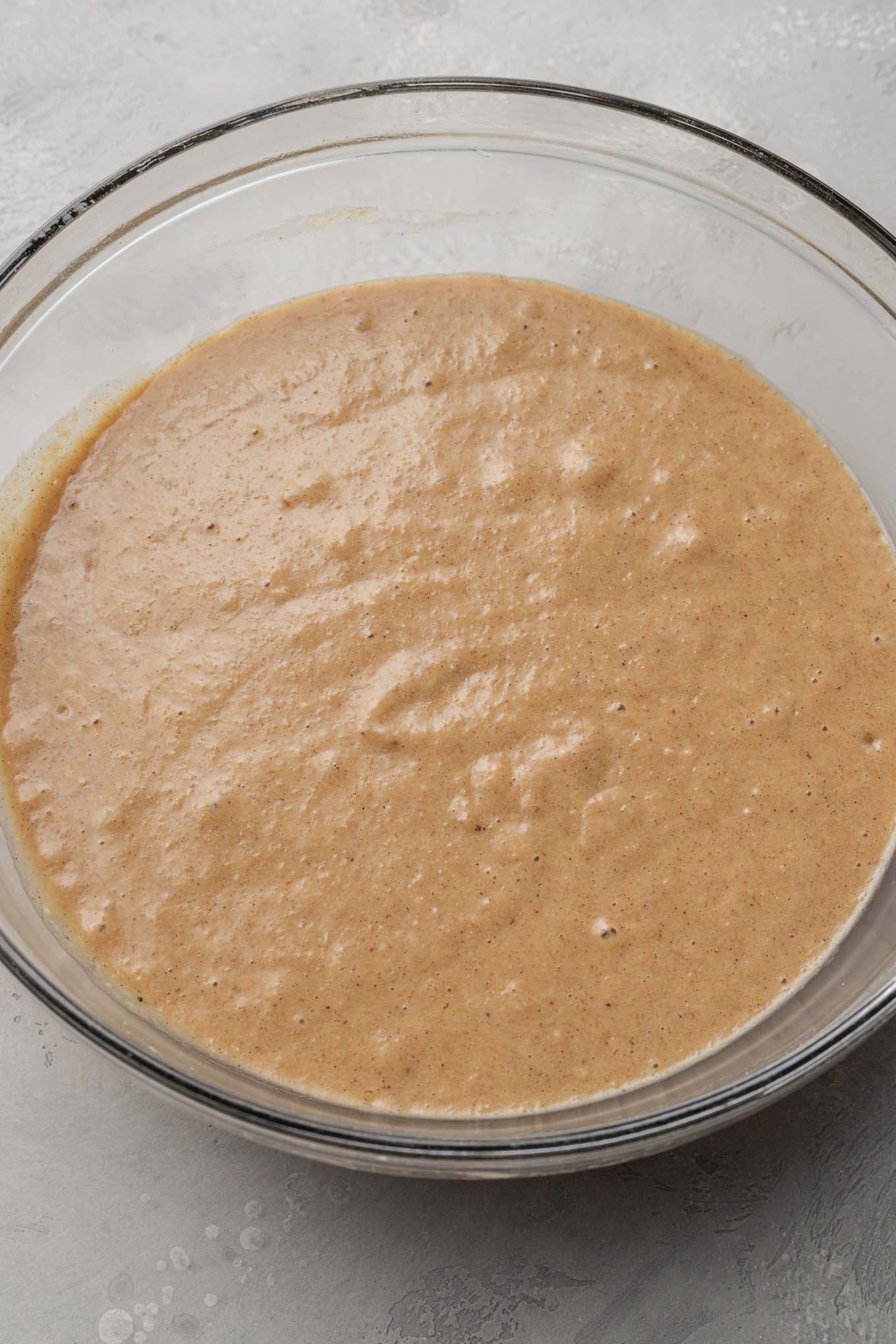 An overhead view of applesauce cake batter, in a glass mixing bowl. 