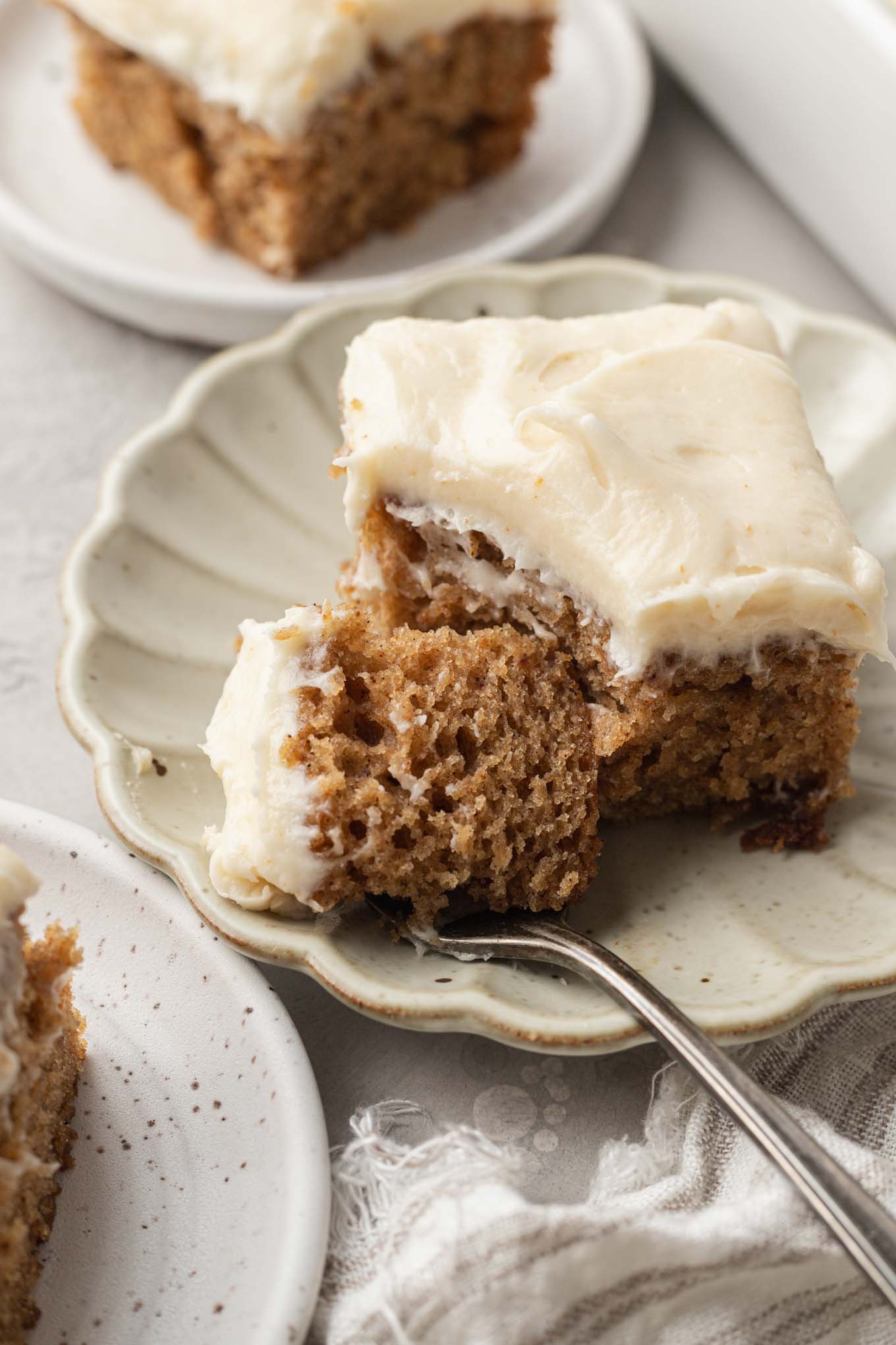 A slice of applesauce cake on a scalloped dessert plate. A bite rests on a fork. 