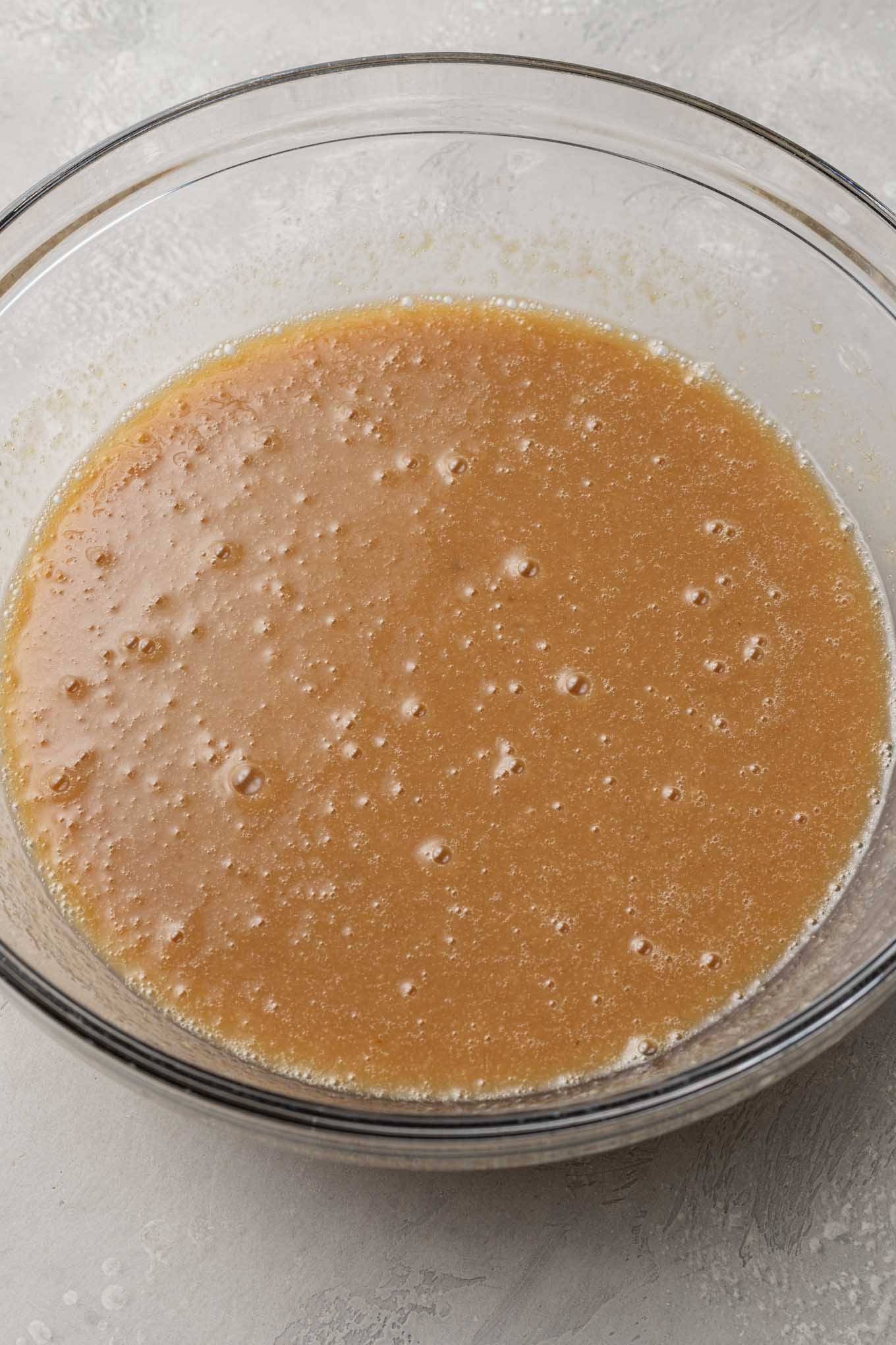 An overhead view of the wet ingredients for applesauce cake, in a glass mixing bowl. 