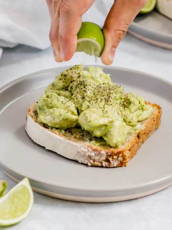 A slice of bread topped with avocado chicken salad. Fresh lime juice is being squeezed on top of it.