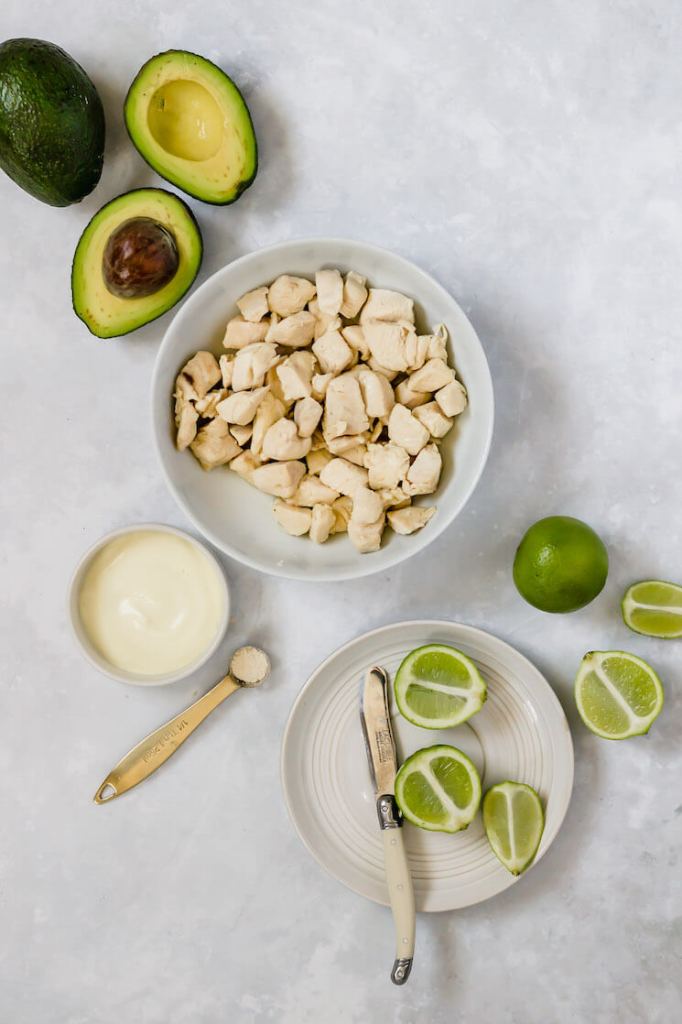 The ingredients needed to make avocado chicken salad in different bowls and measuring cups.