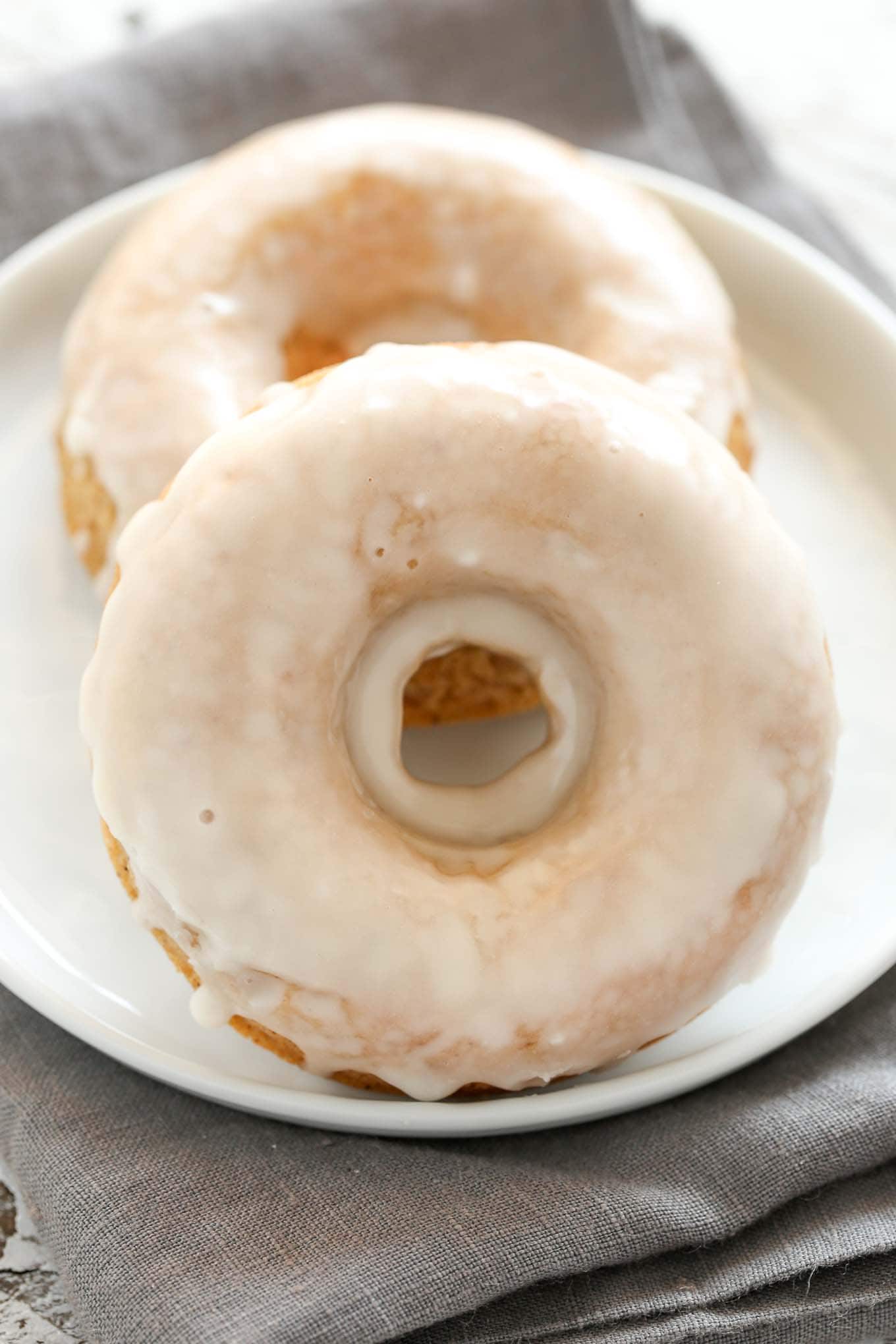 Two glazed apple cider donuts on a white plate. 