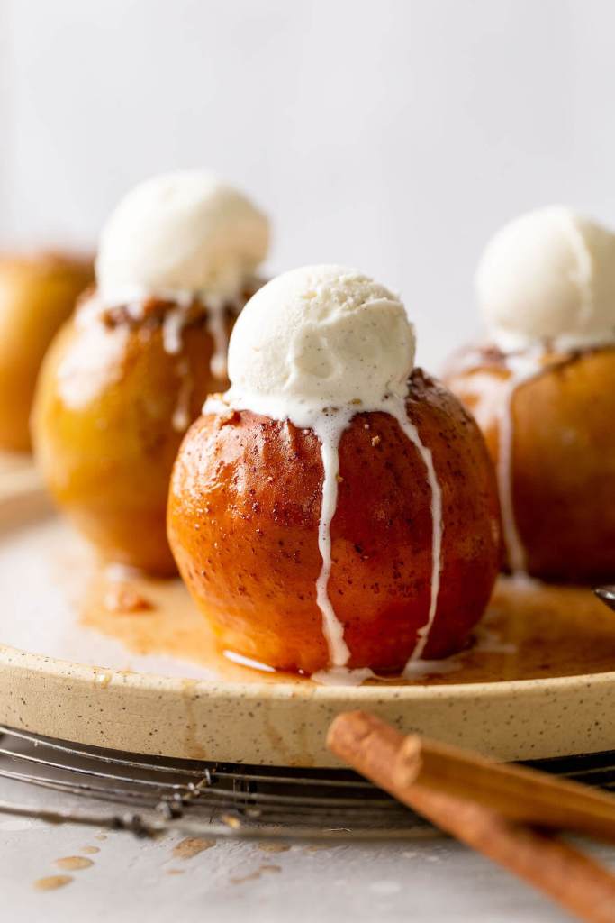 Three stuffed baked apples topped with vanilla ice cream on a speckled white plate. 