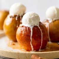 Three baked apples topped with ice cream on a white speckled plate.