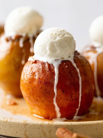 Three baked apples topped with ice cream on a white speckled plate.