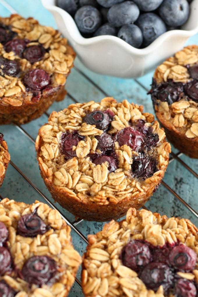 Healthy blueberry baked oatmeal cups cooling on a wire rack. A bowl of berries rests on the side. 