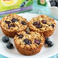 Three blueberry baked oatmeal cups on a white plate with fresh berries.