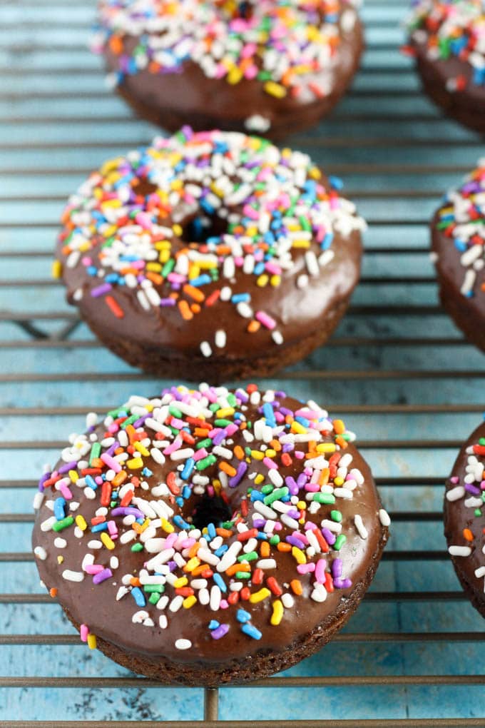 Baked chocolate frosted donuts on a wire cooling rack. Each donut is topped with sprinkles. 