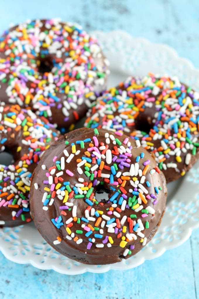 Four chocolate frosted donuts on a white dessert plate. Each donut is coated in sprinkles. 