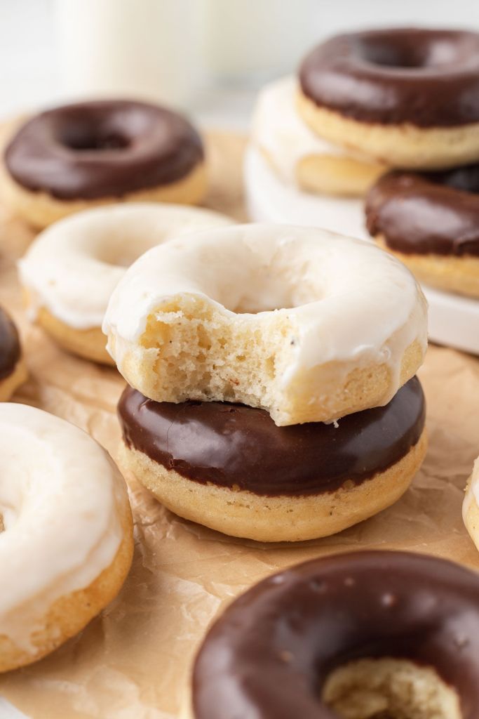 Baked cake donuts on parchment paper. Two donuts are stacked atop each other in the center. 