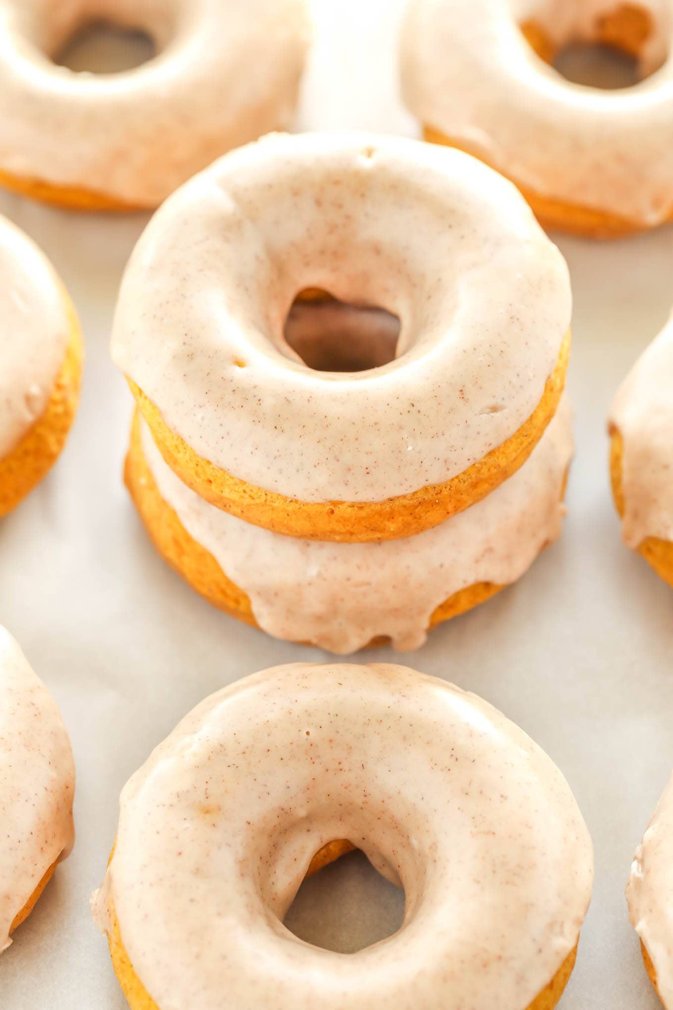 A stack of two baked pumpkin donuts. Additional donuts surround the stack.