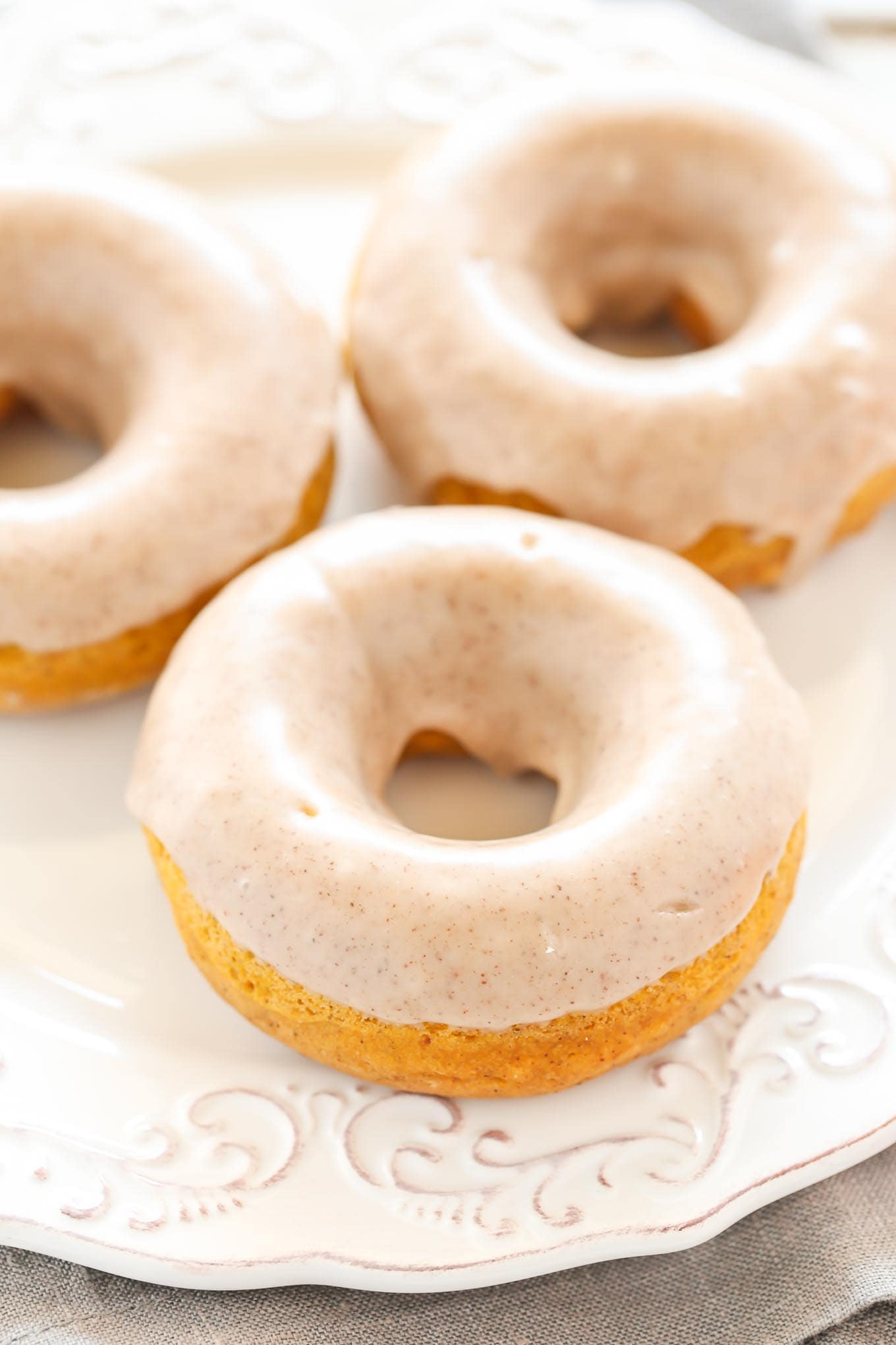 Three pumpkin donuts topped with maple glaze on a white plate. 