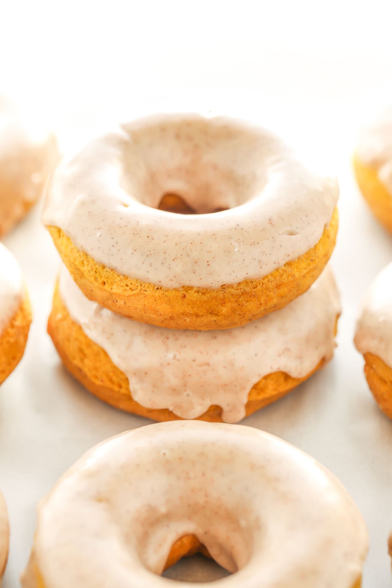 A stack of two pumpkin donuts. Additional donuts surround the stack. 