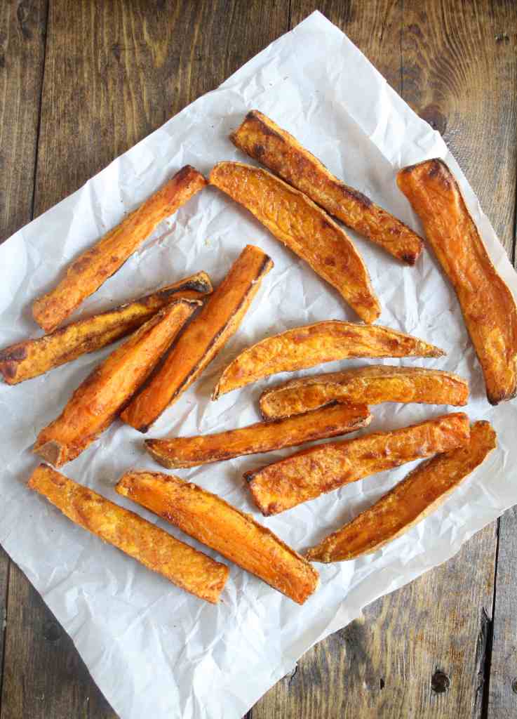 Overhead view of oven baked sweet potato fries on a square of parchment paper. 