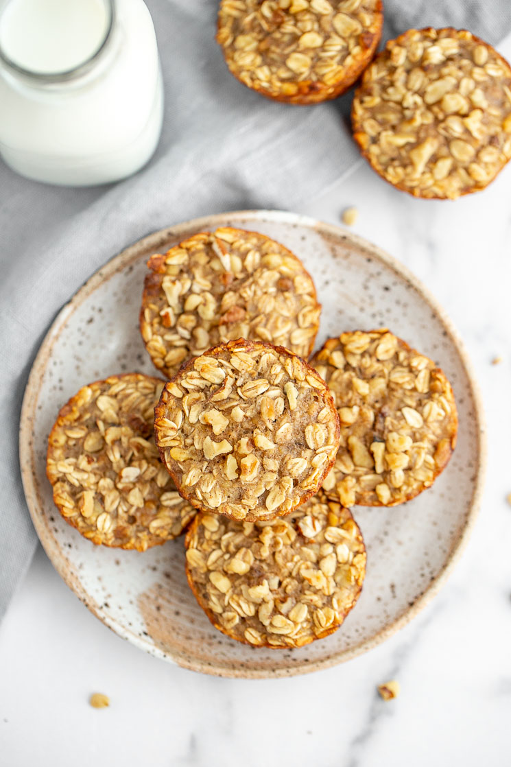 A speckled plate holding banana baked oatmeal cups on top of a marble surface with more oatmeal cups and milk in the background.