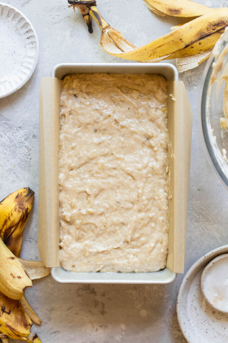 A loaf pan lined with parchment paper holding batter ready to be put into the oven.