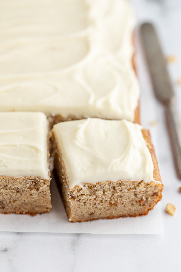 A finished banana cake, resting on a marble surface, with one piece cut and pulled away to show the texture of the cake. 