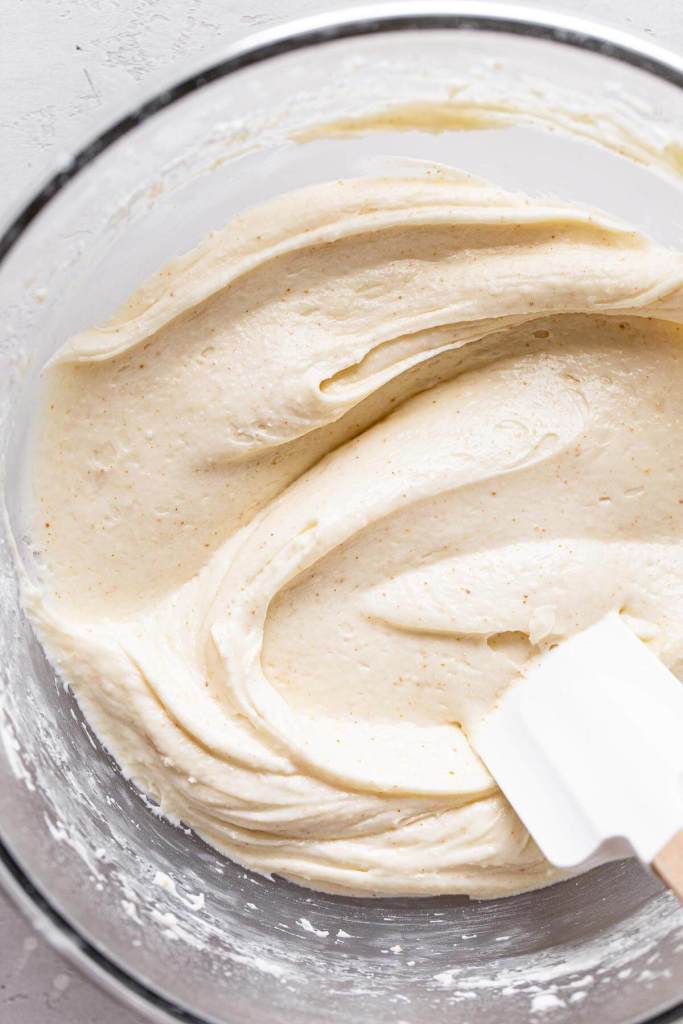 An overhead view of a glass mixing bowl full of brown butter cream cheese frosting. A rubber spatula rests in the bowl. 