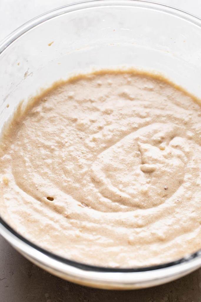 A glass mixing bowl full of banana cupcake batter. 