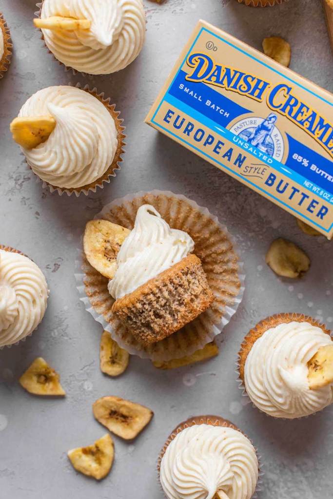 An overhead view of frosted banana cupcakes with a package of Danish Creamery butter. One cupcake is lying on its side. 