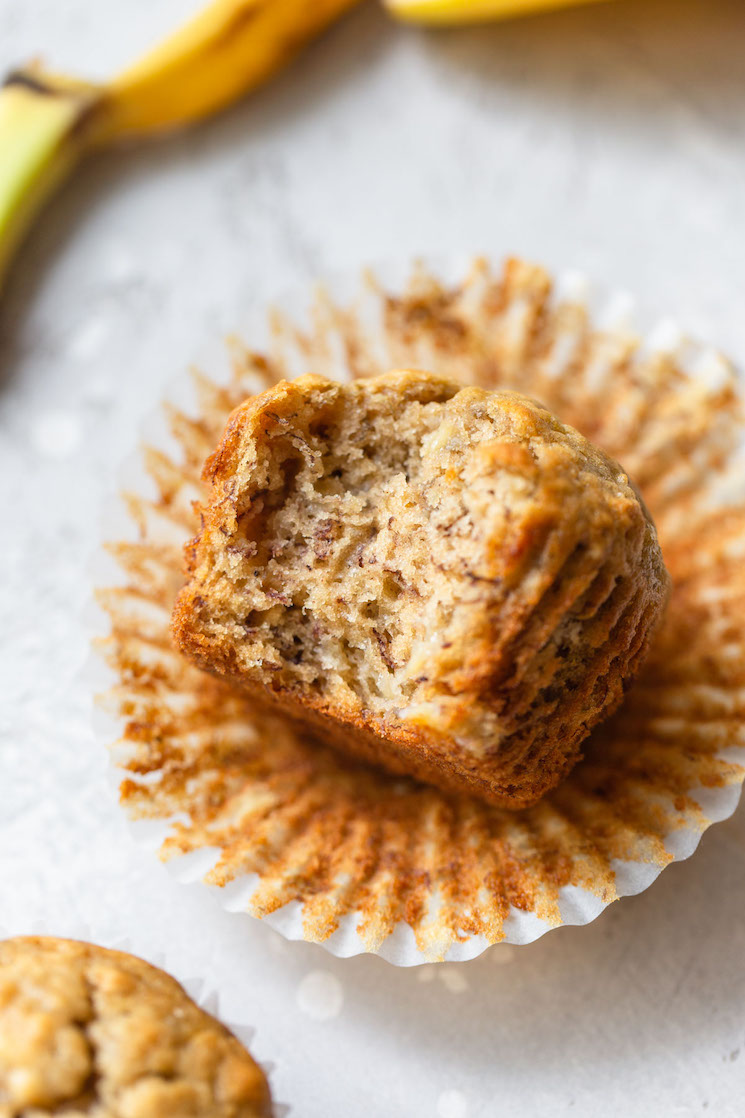 A single banana muffin resting in its wrapper on its side with a bite taken out.